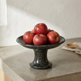 CRUSOË black marble pedestal cake stand with red apples on a concrete countertop.