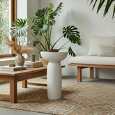 CRUSOË white sculptural pedestal table with a wide bowl top and cylindrical base, styled with a plant and decorative items.